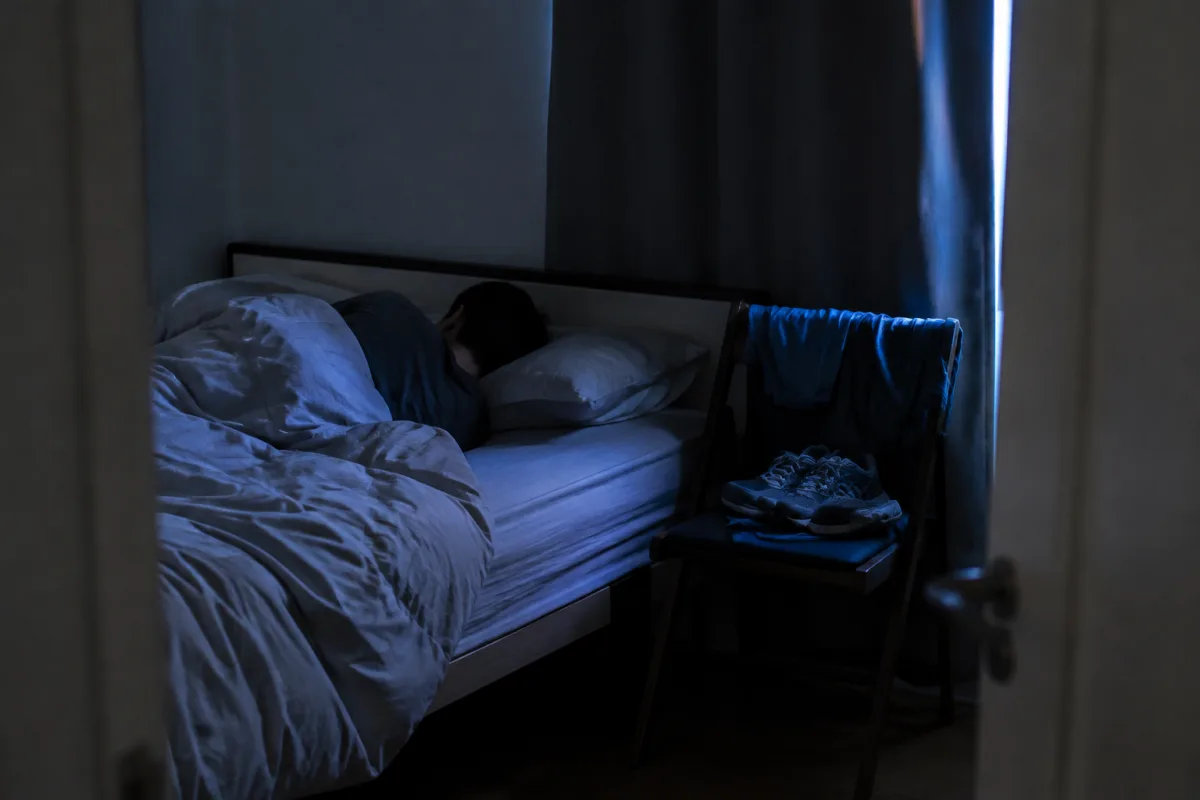Sypialnia przed świtem, osoba śpi pod kołdrą, buty i strój biegowy przygotowane na krześle obok łóżka