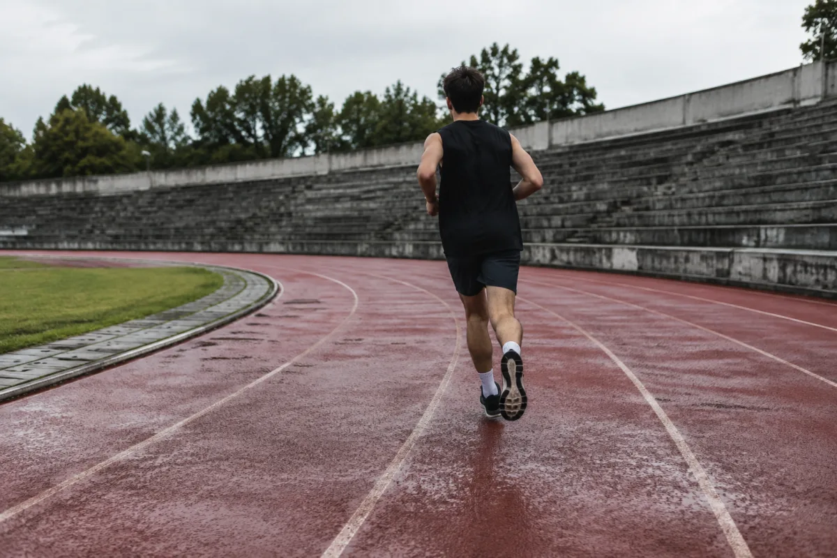 Biegacz na wewnętrznym torze podniszczonej bieżni lekkoatletycznej, pusta trybuna, pochmurny dzień
