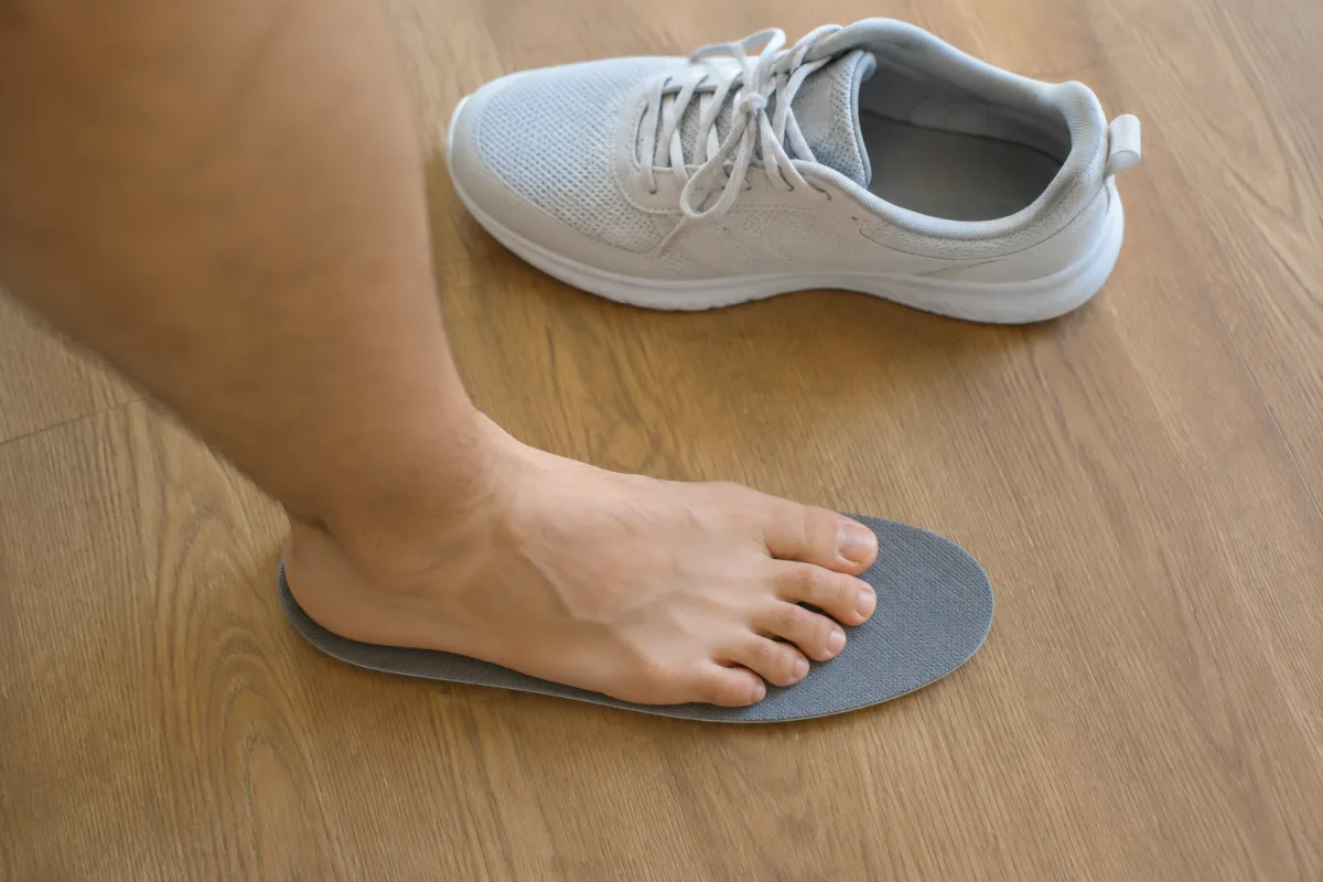 Wkładka wyjęta z buta biegowego leży na drewnianej podłodze, bosa stopa stoi na niej piętą przy tylnej krawędzi, przed palcami widać wyraźny zapas materiału