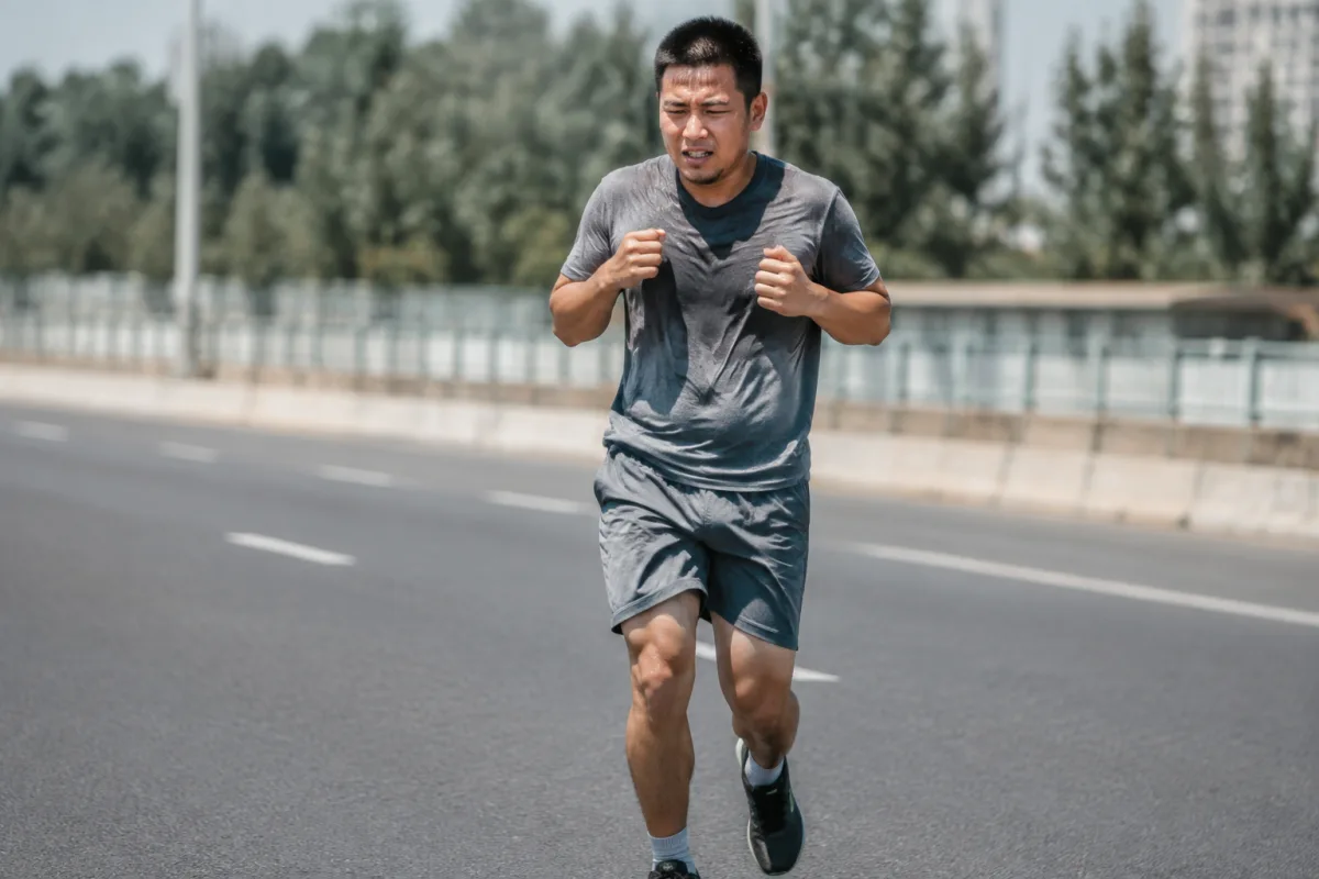 Biegacz amator w końcowej fazie miejskiego półmaratonu, krok wyraźnie krótszy, przedramiona uniesione wyżej przy klatce, twarz skupiona, w tle rozmyta pusta ulica