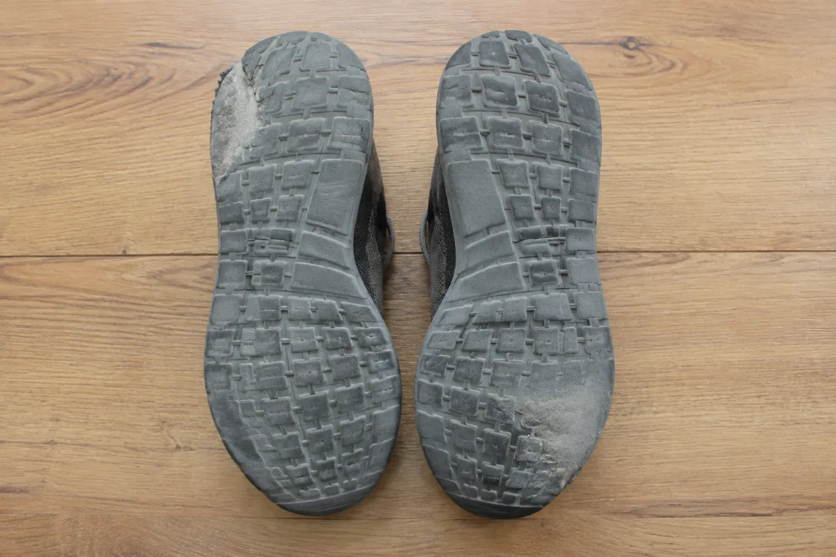 Oba buty jednej pary nieoznakowanych butów biegowych leżące podeszwami do góry obok siebie na drewnianej podłodze, widoczne wytarcia gumy w różnych miejscach na lewym i na prawym bucie