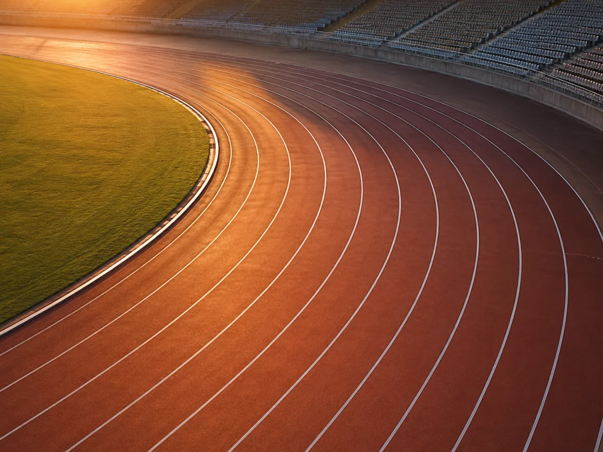 Pusta bieżnia lekkoatletyczna widziana z góry o świcie, wyraźne linie torów i łuk wirażu, brak ludzi