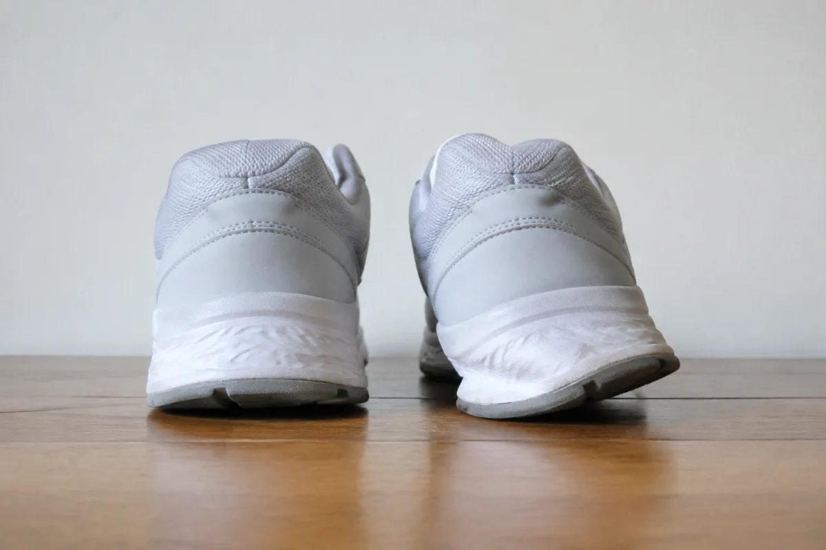 Dwa buty do biegania stojące na płaskim blacie sfotografowane od tyłu na wysokości stołu, prawy but wyraźnie przechylony na zewnątrz